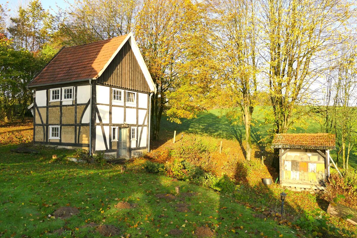 Ein weiß-braunes Fachwerkgebäude auf dem Mühlenhof-Gelände im Herbst, daneben das alte Bienenhaus.